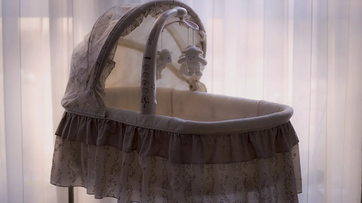 Un berceau vide à capote, avec un mobile de petits moutons en peluche, devant un rideau voilé