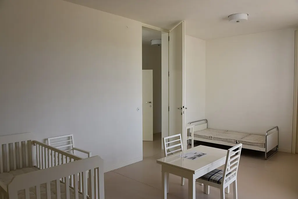 Une chambre d'enfant claire et dépouillée, avec un lit à barreaux vide, une petite table et un lit simple