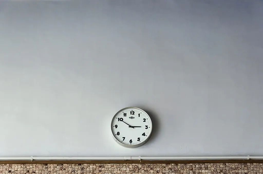 Une horloge ronde et sobre accrochée seule au milieu d'un grand mur blanc