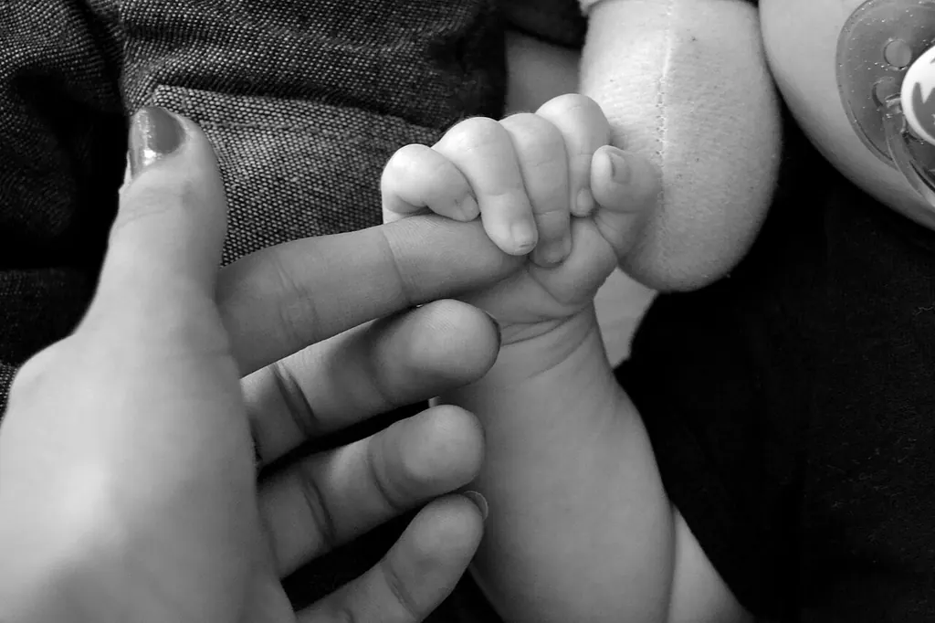 En noir et blanc, un bébé tenu contre un adulte serre fermement l'un de ses doigts dans sa petite main