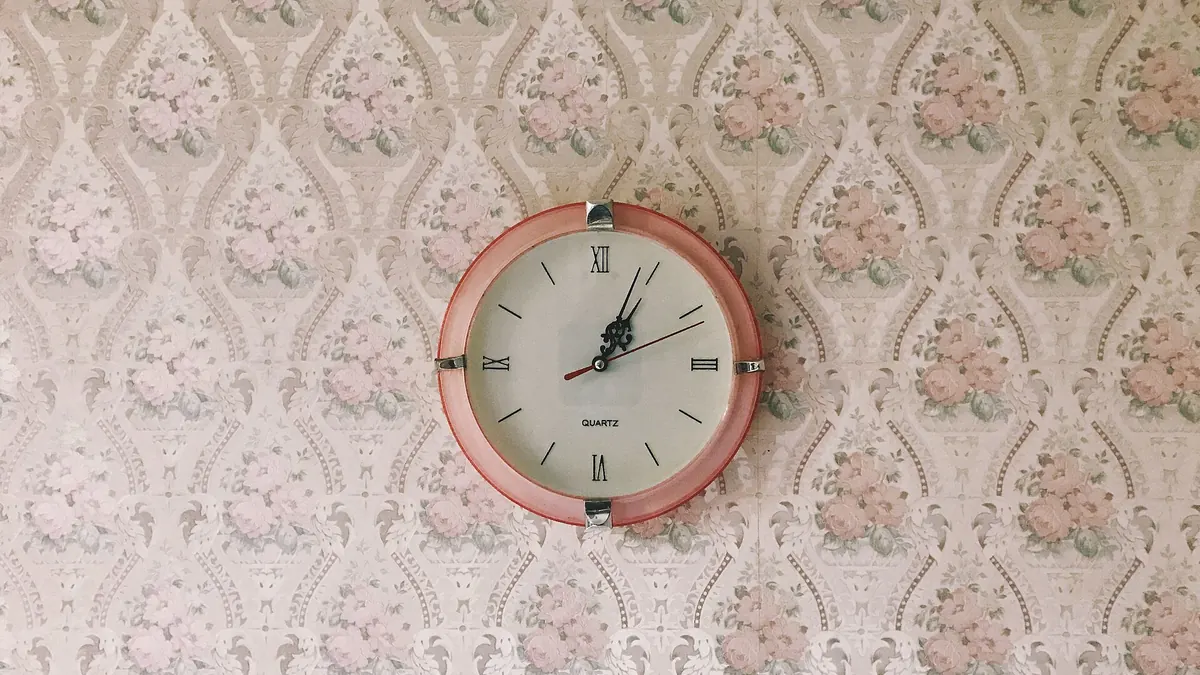 Une horloge murale rose accrochée sur un papier peint à motifs de fleurs