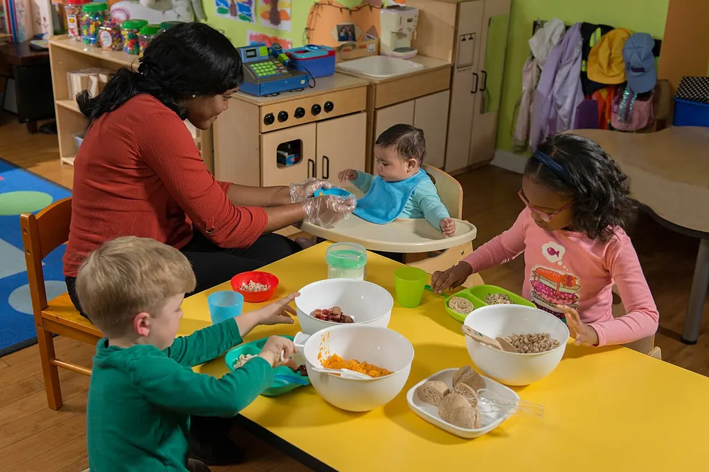 À la crèche, une professionnelle partage un repas avec un bébé en chaise haute et deux jeunes enfants