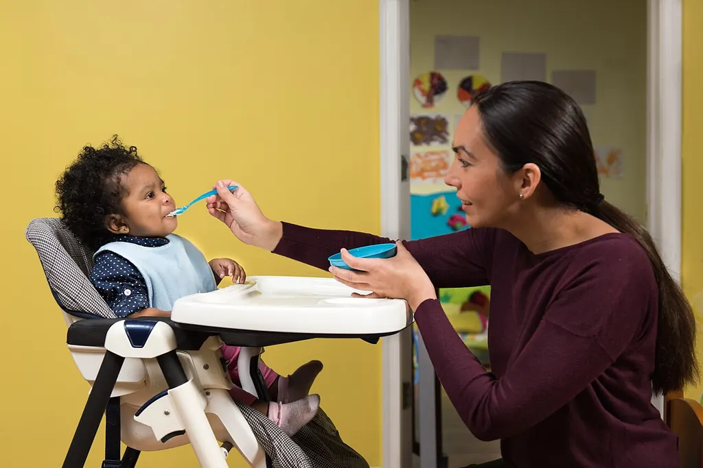 Une femme donne à manger à la cuillère à un bébé installé dans sa chaise haute, en pleine journée
