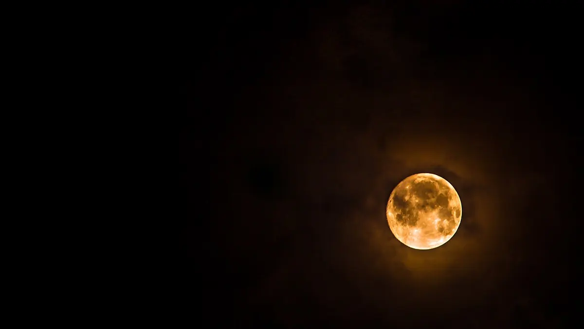 Une lune orangée entourée d'un léger halo, seule dans le ciel noir de la nuit