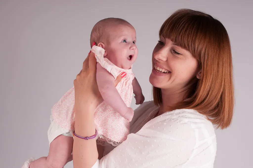 Une jeune femme rieuse soulève devant elle un bébé de quelques mois, bien éveillé