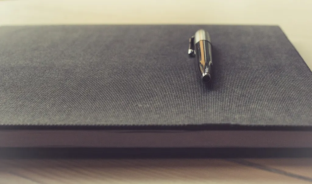 Un stylo posé sur la couverture d'un carnet fermé, sur un bureau