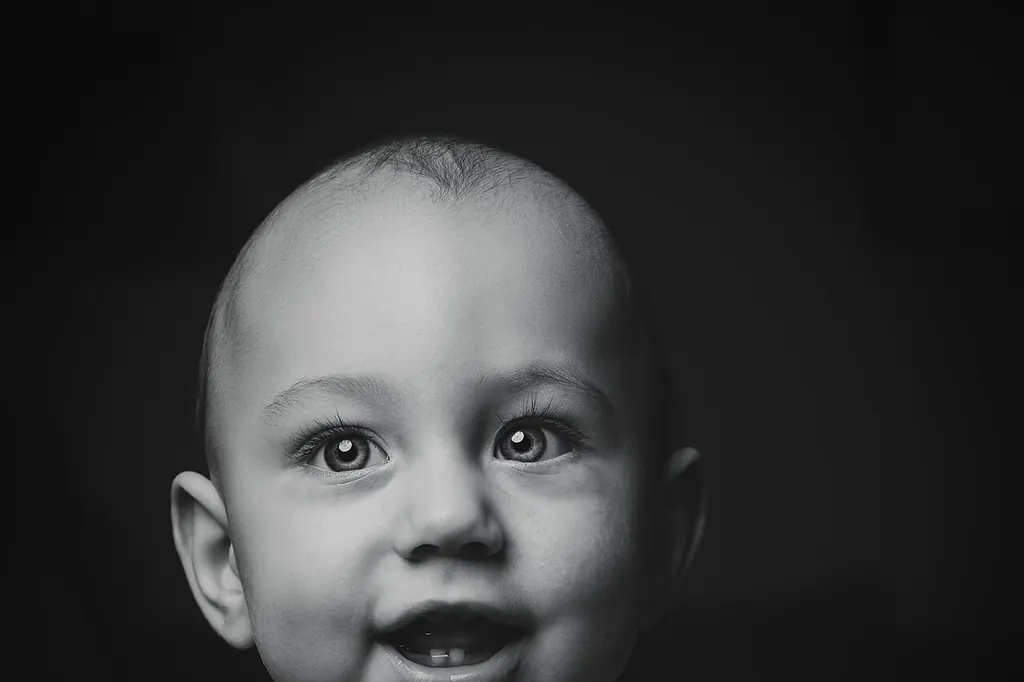En noir et blanc, un bébé bien réveillé sourit, les yeux grands ouverts